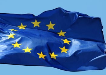 European Union flag waving in the wind against a clear blue sky, blue field with 12 gold stars in a circle tanking motioned by breeze