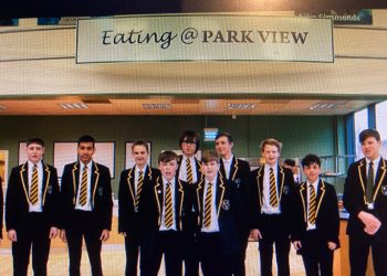 A group of schoolboys in black blazers with striped yellow-and-black ties pose for a photo in a school lobby or cafeteria area under a sign that reads “Eating @ PARK VIEW.”